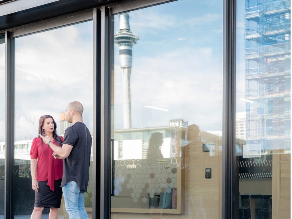 Couple standing in front of a piece of glass, sky tower reflecting from the glass.