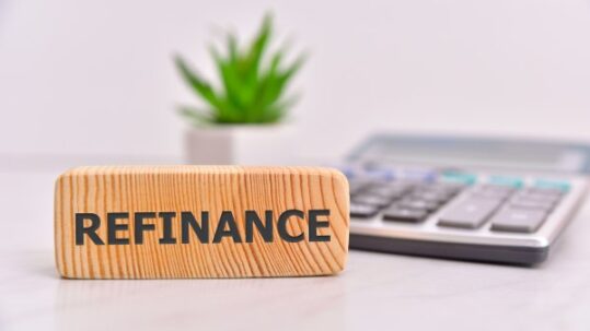 Word “Refinance” on wooden block with calculator in the background